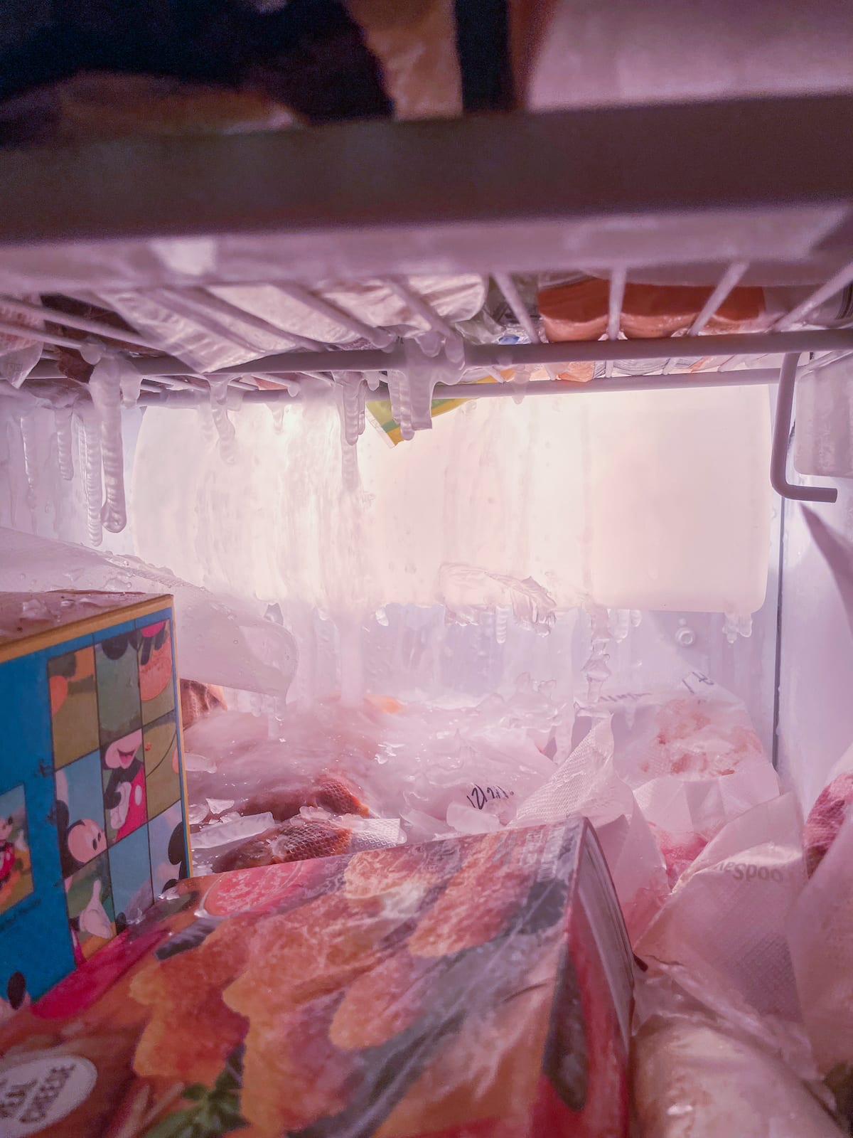 Inside of a freezer with icicles hanging down over frozen food.